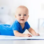 Baby mit blauen Augen und blauem Body liegt auf dem Bauch und entdeckt die Welt.