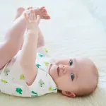 Baby mit blauen Augen in niedlichem Frosch-Body spielt fröhlich auf weicher Decke.