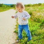 Kind im Alter von ca. 18 Monaten geht frei draußen auf einem Feldweg, erkundet spielerisch seine motorischen Fähigkeiten in der Natur.