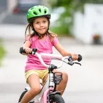 Kind im Alter von 4 bis 6 Jahren fährt sicher mit einem pinken Fahrrad auf zwei Rädern, dabei trägt sie einen grünen Helm