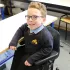 Junge mit Brille sitzt in einem VELA Stuhl in einem Klassenzimmer, trägt Schuluniform