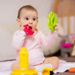 Baby sitzt auf Boden und spielt mit buntem Spielzeug.
